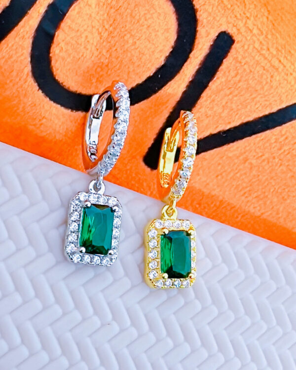huggie hoop earring with dangling emerald color stone in halo setting.