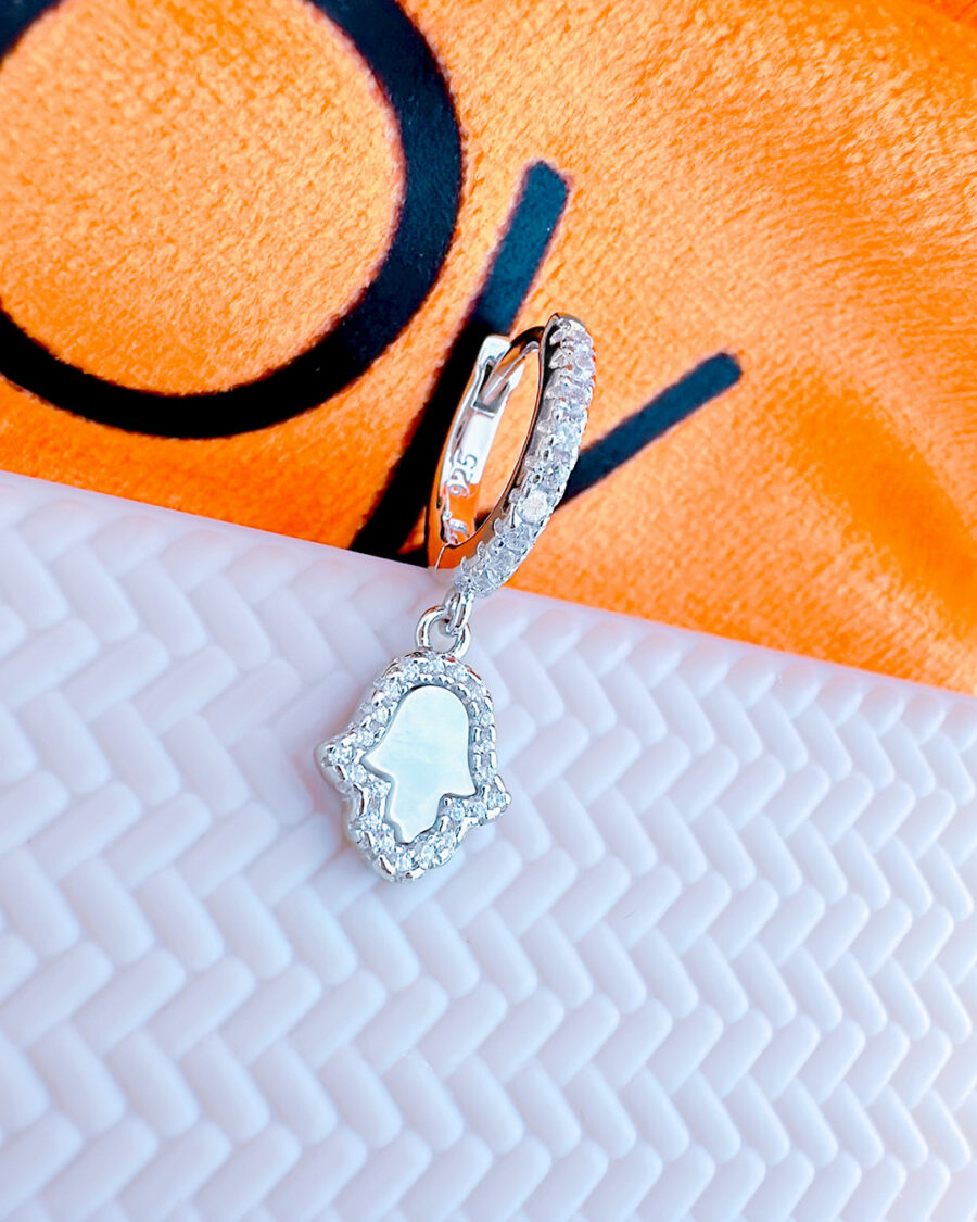 CZ huggie hoop earring with dangling MOF hamsa shape in a halo setting.